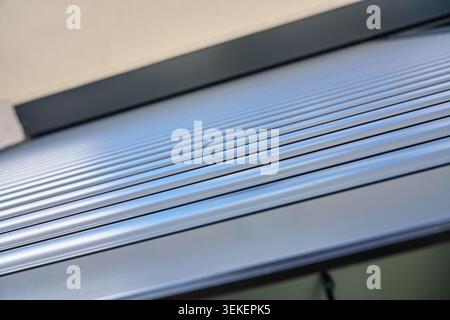 Closeup of a grey exterior roller shutter with horizontal metal slats installed above a modern house window. Stock Photo
