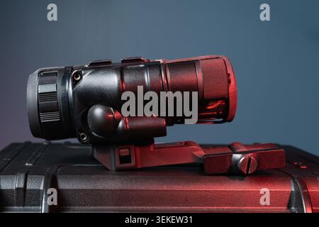 Tactical night vision monocular device mounted on quick detach rifle scope base on protective plastic hard case close up under red light Stock Photo