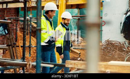 Construction, architect and manager talk on site for project planning, inspection and renovation. Team, men and tablet with blueprint outdoor for Stock Photo