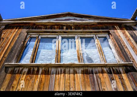 Old wooden house with weathered planks and glass windows. Blue sky above the roofline. Rustic, vintage architectural style Stock Photo