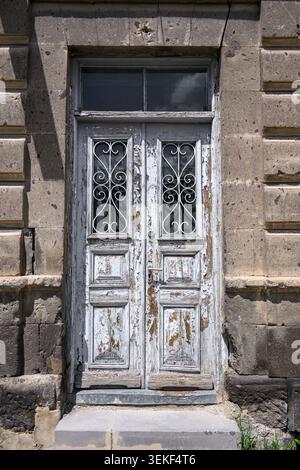Weathered white wooden door with ironwork. Set in stone wall. Door shows peeling paint and aged texture Stock Photo