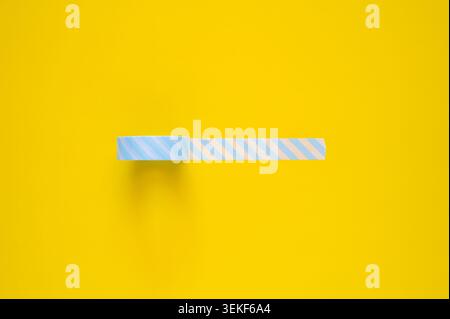 A single roll of light blue and white striped tape partially unrolled on a yellow background. Stock Photo