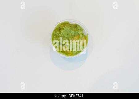 Mashed avocado in a small plastic pot on a white background for poke bowls, salads and healthy takeaway meals. Stock Photo