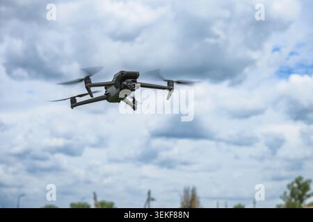 Modern quadcopter drone hovering in the air against dramatic cloudy sky. Unmanned aerial vehicle with camera used for photography, inspection, mapping Stock Photo