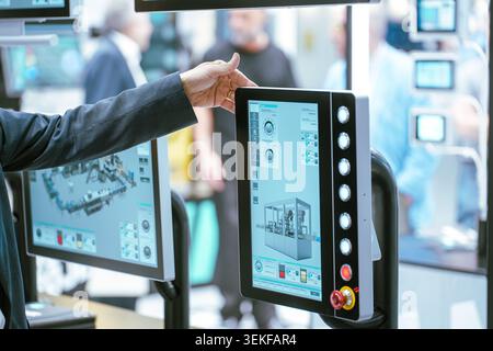 A person points toward an industrial human-machine interface (HMI) monitor displaying manufacturing metrics and diagnostic diagnostics at an automatio Stock Photo