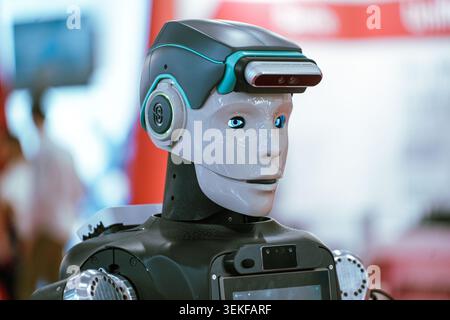 A close-up profile view of an advanced humanoid service robot with illuminated blue eyes and a head-mounted sensor array on display at an automation t Stock Photo