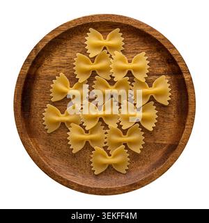 Farfalle pasta arranged in a geometric pattern on a wooden plate viewed from above on white background. Stock Photo