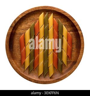 Tricolor penne pasta arranged on a wooden plate in a geometric pattern viewed from above on white background. Stock Photo