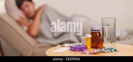Medicine and water on table with sick person blurred in background Stock Photo