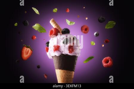 Pink berry ice cream in a chocolate-dipped cone, surrounded by floating raspberries, blueberries, blackberries, strawberries, and mint leaves on a pur Stock Photo