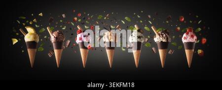 A lineup of colorful ice cream cones with assorted flavors, toppings, fruits, chocolate, and mint, surrounded by floating ingredients on a dark backgr Stock Photo