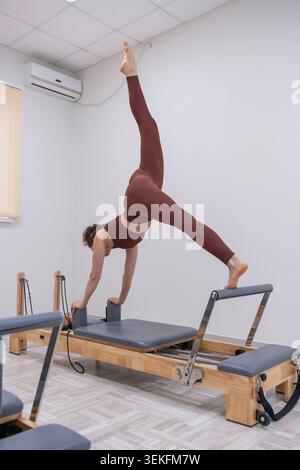 Pilates reformer workout woman practicing advanced yoga split on professional machine in a bright studio Stock Photo
