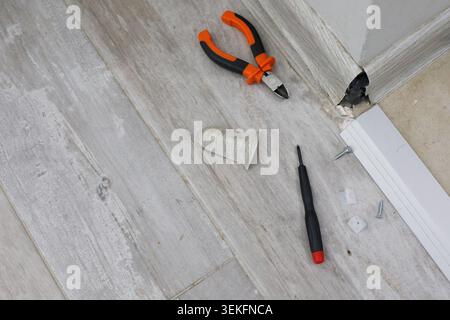Tools are laid out on a wooden floor near a wall. Pliers, screwdrivers, and some small parts are visible. This scene shows a home repair project in pr Stock Photo
