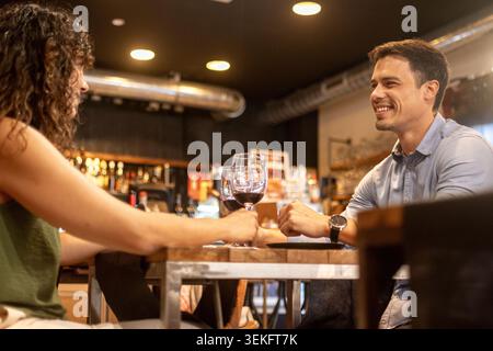 Young couple sharing quality time together over glasses of red wine in a modern restaurant. Man smiling while talking with his partner during a relaxe Stock Photo