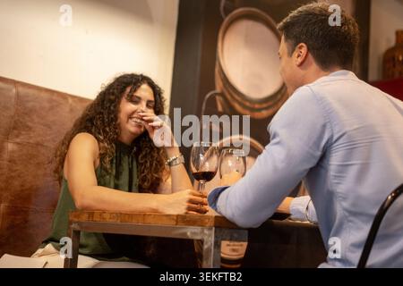 Happy couple sharing a relaxed conversation over glasses of red wine in a cozy restaurant. Stock Photo