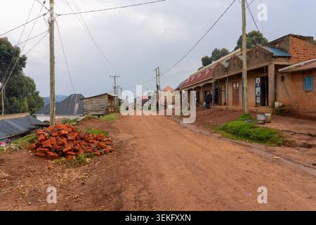 A pile of bricks in an Uganda rural village street showing a vibrant local life with people walking and standing near humble shops and houses built fr Stock Photo