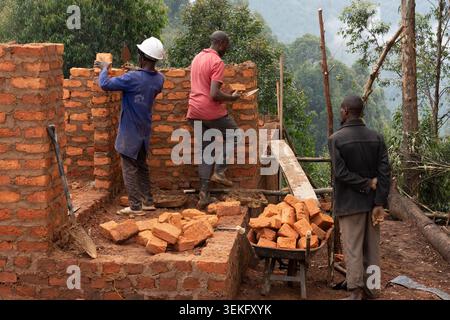African construction workers carefully laying bricks to build a new structure on a hillside, using traditional methods and materials for a community d Stock Photo