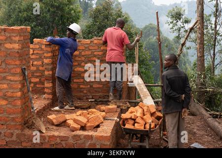African construction workers carefully laying bricks to build a new structure on a hillside, using traditional methods and materials for a community d Stock Photo