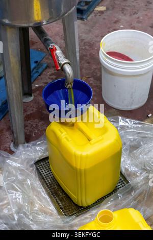 Olive oil flows from a metal spout through a blue funnel into large 16L yellow plastic containers on a factory line during industrial packaging and fi Stock Photo