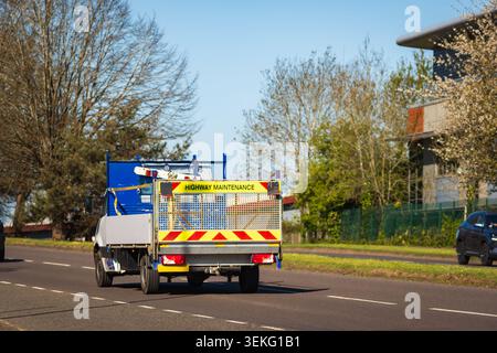 A green and beige dump truck drives along a two-lane country road with a passing car in the opposite lane, trees and spring foliage lining the roadsid Stock Photo