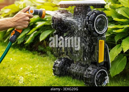 Cleaning robotic lawn mower. Washing with water from garden hose Stock Photo