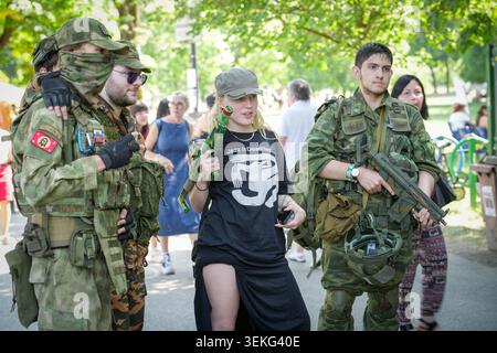 A group of participants dressed in military camouflage gear and holding replica firearms converse along a pathway during an outdoor public event Stock Photo