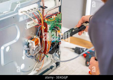 Technician testing electronic components and wiring inside disassembled electric oven. Appliance diagnostics and professional repair service concept Stock Photo