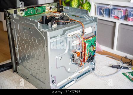 Disassembled electric oven during repair with removed electronic module and tools. Home appliance maintenance concept Stock Photo