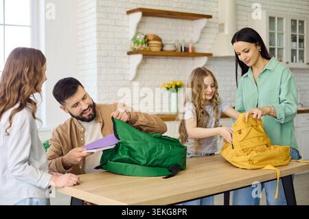 Parents and schoolgirls packing backpacks at home kitchen for back to school Stock Photo