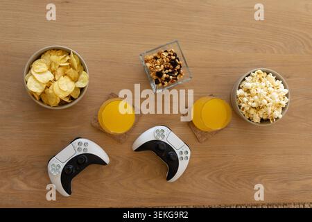 Top-down view showing wireless controllers on light table with juice on coasters chips popcorn nuts Stock Photo