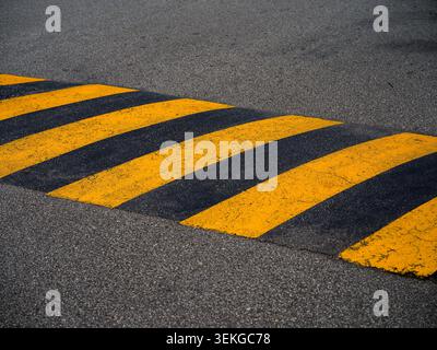 Yellow and Black Striped Speed Bump Painted on an Asphalt Road Surface Stock Photo