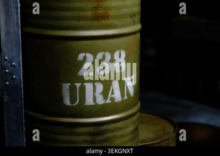 Green metal barrel labeled with 238 URAN, positioned in a dimly lit industrial environment, showcasing weathered surface and storage context Stock Photo