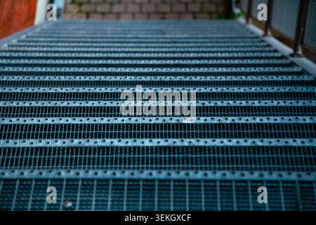 This professional close up outdoor photograph captures the detailed and modern texture of industrial metal stairs. The camera is positioned at a low angle focusing closely on the durable steel grating Stock Photo