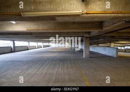Empty concrete multi story car park with fluorescent lights, structural beams, and a striped floor Stock Photo