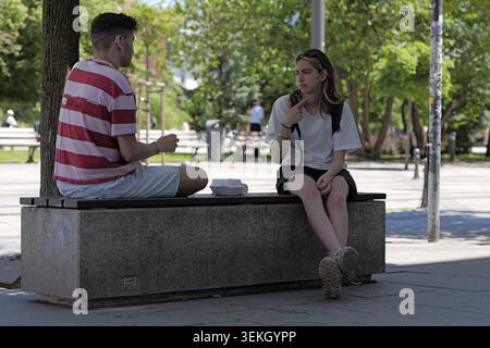Young woman actively communicating using sign language with a man while sitting on a park bench, representing concepts of inclusion, accessibility, an Stock Photo