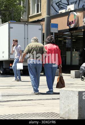 Senior couple walking arm in arm down a sunny city street, enjoying supportive companionship and relaxed togetherness during a leisurely daytime strol Stock Photo