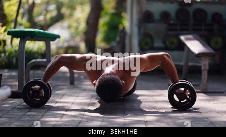 Male athlete doing push ups with dumbbells at outdoor street workout gym Stock Photo