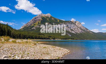 Mount Kidd towering over a clear alpine lake surrounded by pine forest Stock Photo