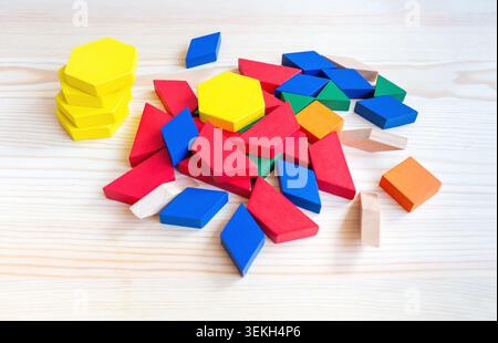 Colorful wooden geometric shapes including hexagons, squares, and triangles scattered on a light wooden surface, ideal for educational play and Stock Photo