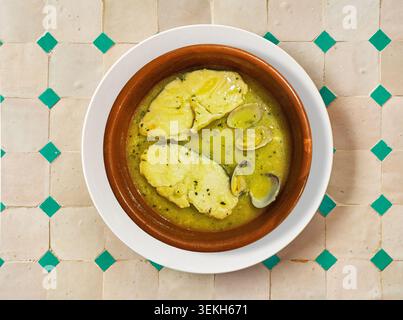 Traditional Basque hake in green sauce served with clams in a clay pot. Top view of Merluza a la vasca or salsa verde, a classic Spanish seafood dish. Stock Photo