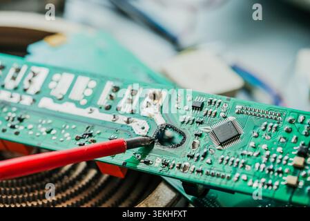 Close-up of a technician using a soldering iron to repair a damaged electronic circuit board, showcasing the intricate components and the precision required in electronics repair Stock Photo