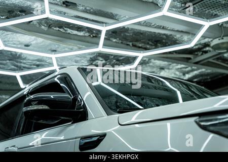 Close view of a white sports car inside a modern indoor setting, with strong reflections from geometric ceiling lights across the body and windshield Stock Photo
