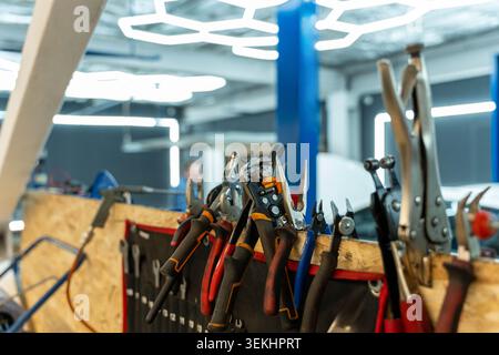 Assorted hand tools hang from and rest on a cluttered workbench in a bright modern workshop, with pliers, cutters, wrenches, and screwdrivers in the Stock Photo