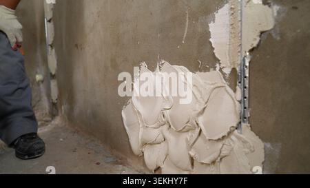 Construction worker applying plaster on wall using corner trowel Stock Photo