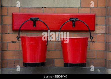 Traditional red fire buckets filled with sand on a UK steam railway platform, reflecting historic railway safety equipment and heritage transport Stock Photo