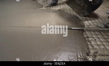 Pouring wet concrete screed onto wire mesh reinforcement for floor construction Stock Photo