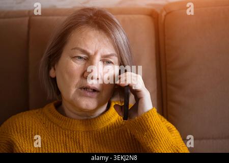 Concerned senior woman talking on mobile phone while sitting on a sofa at home Stock Photo