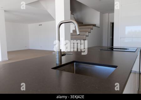 A contemporary kitchen island features a sleek faucet and integrated sink, with a modern staircase visible in the background Stock Photo