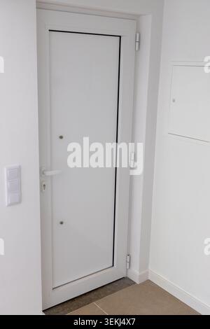 A clean and contemporary white door with a silver handle and visible hinges, set against a textured wall and tiled floor Stock Photo