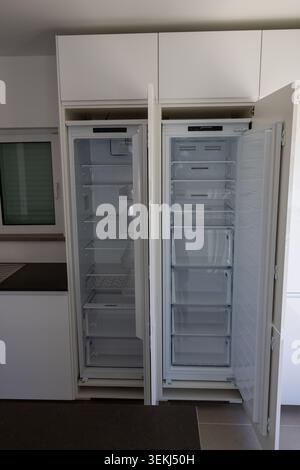 An empty, clean, tall white refrigerator and freezer unit stand open in a contemporary kitchen setting, showcasing their interior storage Stock Photo